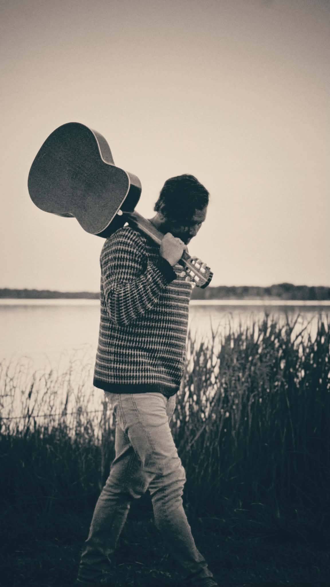 Klas Österman med gitarren över axeln, vid vattnet i skymningen